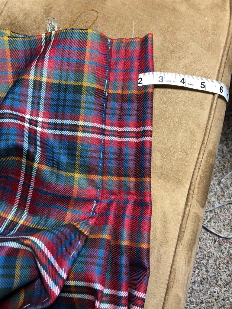 three pleats sewn on a kilt with a tape measure sticking out of the opening for a strap