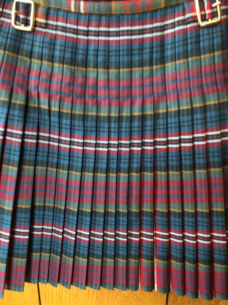 A kilt in MacPherson red muted tartan showing pleats pleated to the double blue stripe
